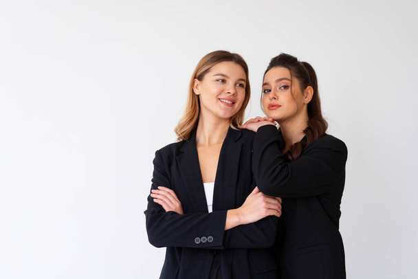 Concept of partnership in business. Two Young businesswoman dressed black formal suit standing studio isolated white background. Brunette woman put her hands on the shoulders of her friend. - Фото, зображення