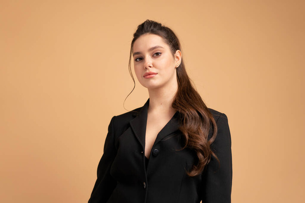 Young business woman close up portrait dressed black jacket standing studio isolated on color background. Caucasian female business person looking at camera with serious face. Medium shoot - 写真・画像