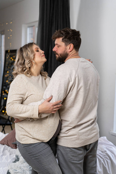 Happy family concept. Husband hug belly pregnant wife standing indoor living room near sofa Caucasian man and woman pregnancy and new life concept. Love and care  - Valokuva, kuva