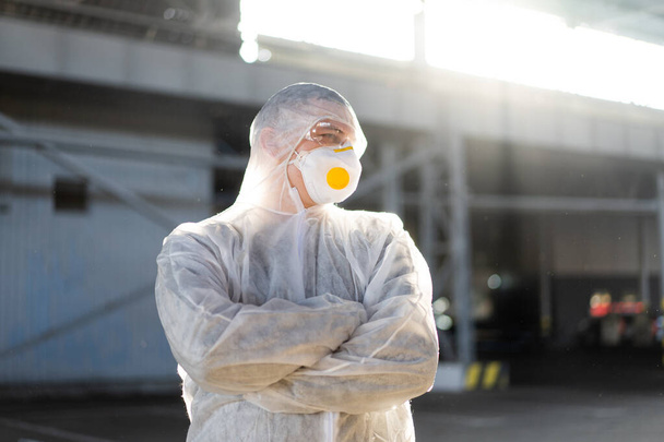 COVID-19 coronavirus doctor standing hospital parking dressed white protective overalls hazmat suit. Infectious disease pandemic medical worker front line, outbreak. Male medical worker medium shoot - Foto, imagen