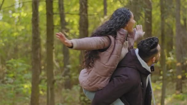 Jonge man houdt zijn vriendin spinnen gelukkig meisje zit op vriendjes rug met armen uit naar zij knuffelen glimlachen genieten tijd doorgebracht samen romantisch date buiten paar in liefde wandelen in park - Video