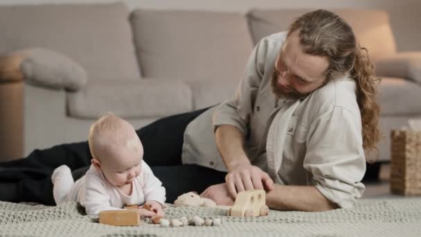 Mutlu yetişkin baba, yeni doğmuş bebek bebeğe yardım ediyor. Oğlu, yere bakan babasıyla oyuncak oynuyor. Küçük kız, evde oyun kurucu olarak eğleniyor. Çocuk gelişimi kavramı - Video, Çekim