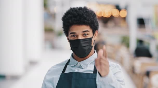 Friendly african masked guy male waiter salesman man in medical face protective mask restaurant cafe kitchen bar worker pointing hey you at camera welcoming gesture come here approach welcome inviting - Footage, Video