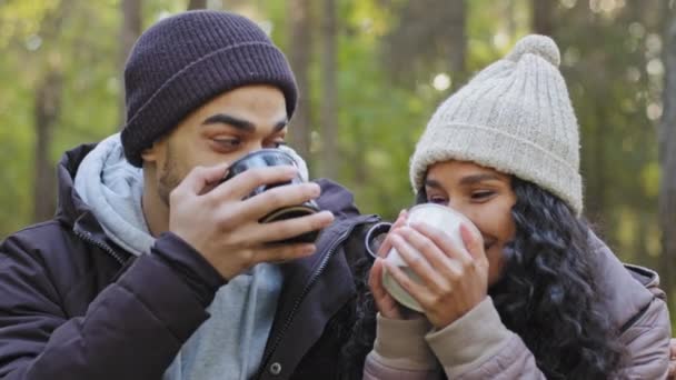 Close-up jong getrouwd stel toeristen ontspannen in de natuur in de herfst hout verwarmen met warme drank drinken warme thee kijken naar elkaar met een blik van liefde glimlachen gevoel gelukkig knuffelen genieten van wandeling - Video