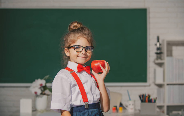 School child hold apple with funny expression against blackboard. Kids education and knowledge. - Photo, Image