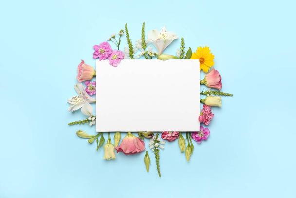 Σύνθεση με λευκή κάρτα και διάφορα λουλούδια σε μπλε φόντο - Φωτογραφία, εικόνα