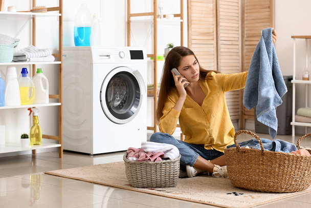 Hermosa ama de casa con lavandería y cestas de mimbre hablando por teléfono móvil en casa - Foto, Imagen