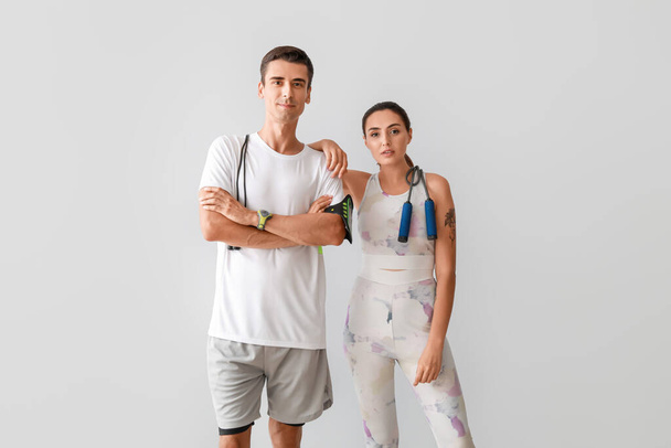 Sporty young couple with skipping ropes on grey background - Photo, image