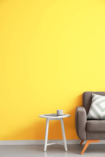 Table basse avec tasse, magazine et fauteuil doux près du mur jaune - Photo, image