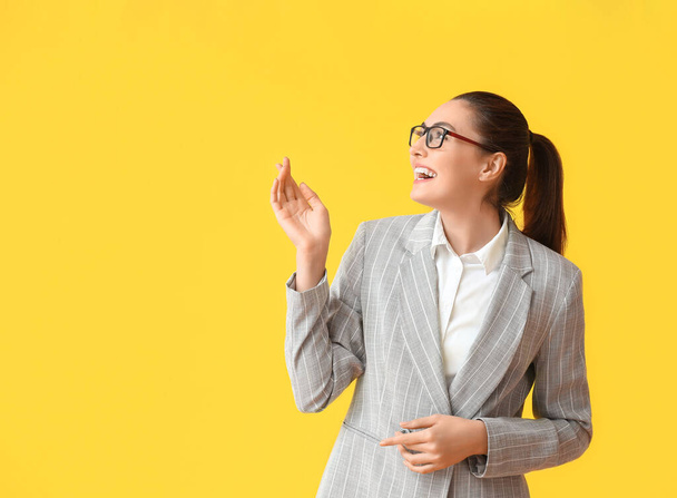 Happy young businesswoman in eyeglasses on yellow background - 写真・画像