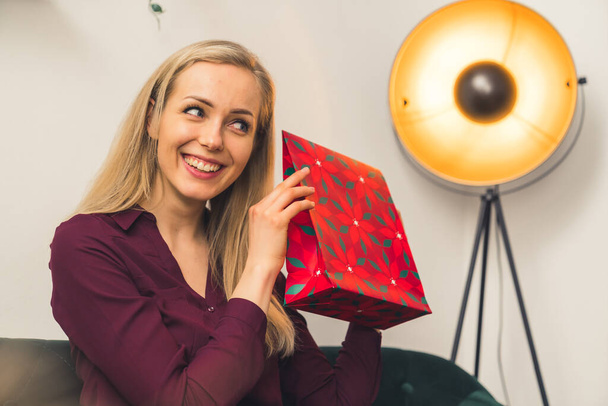 its time to open gifts - an attractive blonde European girl holding a present and smiling medium closeup studio shot indoors wellbeing concept - Photo, Image