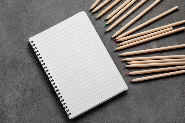 Colorful pencils and blank notebook on dark grunge background - Photo, Image