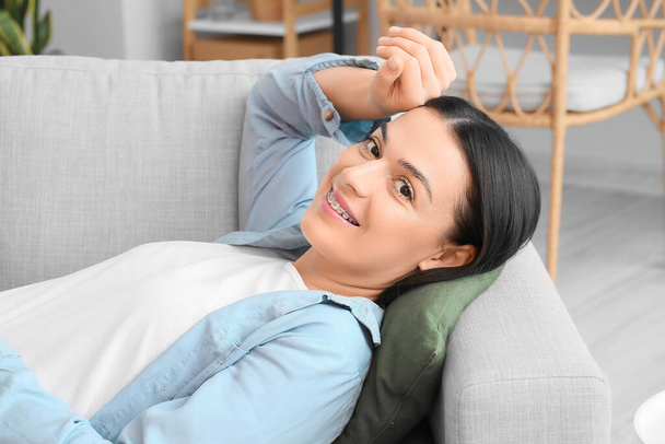 Beautiful woman with dental braces lying on sofa at home - Фото, зображення