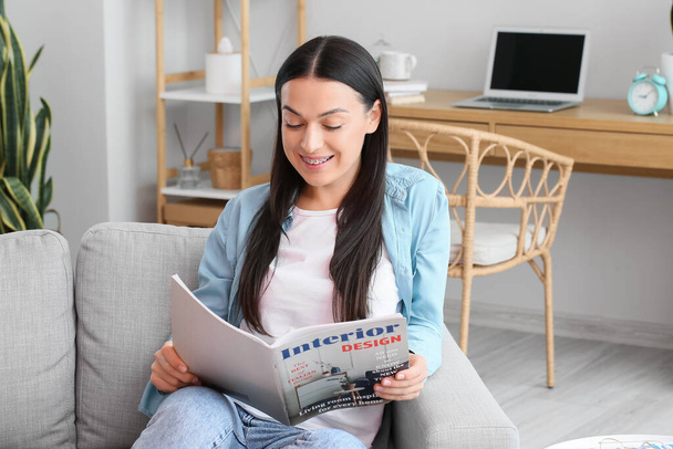 Beautiful woman with dental braces reading magazine on sofa at home - Photo, Image