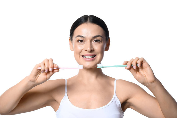 Beautiful woman with dental braces and tooth brushes on white background - Foto, Imagem