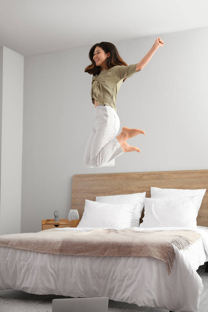 Молодая азиатка босиком прыгает на кровати дома - Фото, изображение