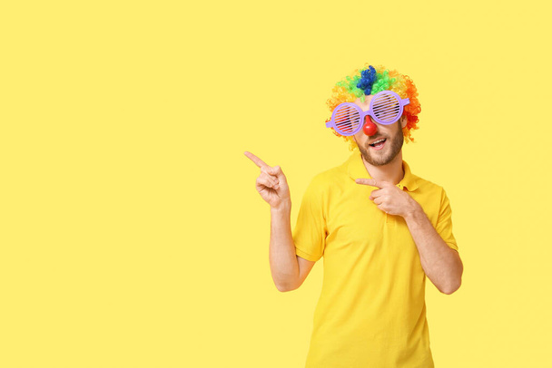 Funny young man in disguise showing something on yellow background. April fools' day celebration - Photo, Image