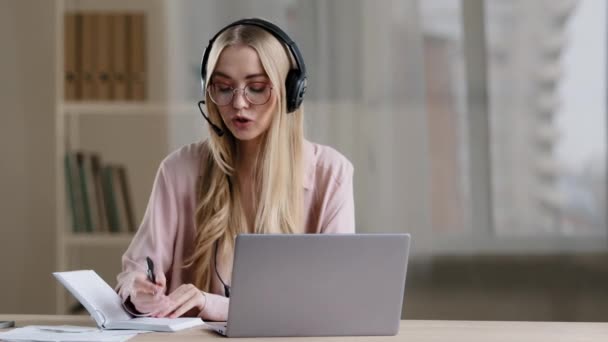 Caucasian girl student online teacher mentor psychologist specialist therapist businesswoman in headset headphones has video call patient consultation remote lawyer e-learning woman writes in notebook - Footage, Video