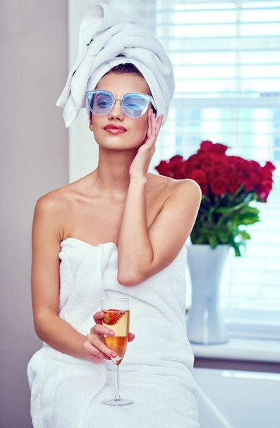 Relaxing like a royal. Shot of an attractive young woman enjoying a glass of champagne while going through her morning routine. - Foto, immagini