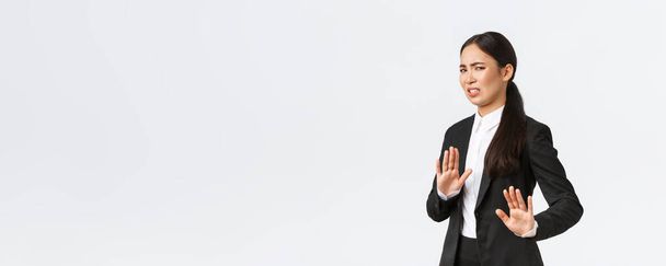Displeased asian businesswoman avoiding risky suggestions, shaking hands in refusal, rejecting disgusting strange offer. Saleswoman grimacing from aversion and step away, white background - Фото, изображение