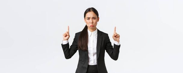 Zklamaný trucující asijské podnikatelky v obleku stěžuje a trucuje z neúspěchu, ukazuje prsty nahoru, šklebící se nespokojenost, pocit z lítosti, stojící bílé pozadí - Fotografie, Obrázek