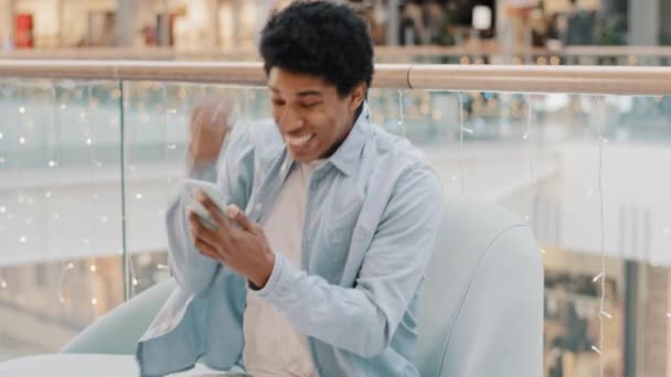 Afrikai srác felhasználó online fogadás mobil játék győzelem ül beltérben telefon siker igen gesztus győzelem javaslat ember kap sms üzenet lehetőséget okostelefon férfi győztes ünnepli győzelem  - Felvétel, videó