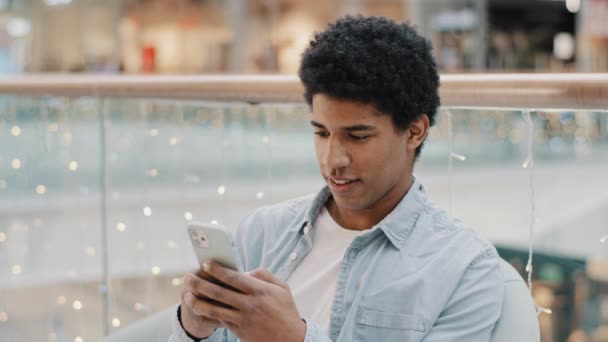 Afrikalı odaklı milenyum adamı, kapalı mekanda oturup mobil sohbet uygulamasını araklıyor online alışveriş oyunu, akıllı telefon sohbetleri, ücretsiz Wi-Fi kullanıcı sohbet sosyal medya.  - Video, Çekim