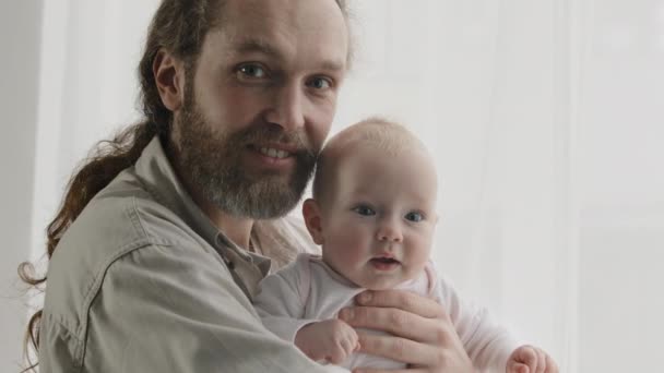 Rodinný portrét usmívající se běloch vousatý otec otec muž drží objímání malé novorozeně dívka chlapec dcera syn dívá na kameru usmívá pózování doma. Detailní záběr tatínek objímající adoptované dítě - Záběry, video