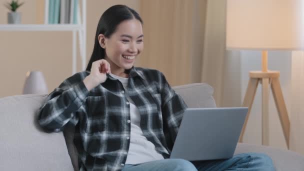 Asijské usmívající se podnikatelka na volné noze student on-line učitel psycholog dívka žena sedí na pohovce doma dálkové mluvení video hovor konference app chat mluví na webkameru mává ahoj konzultace - Záběry, video