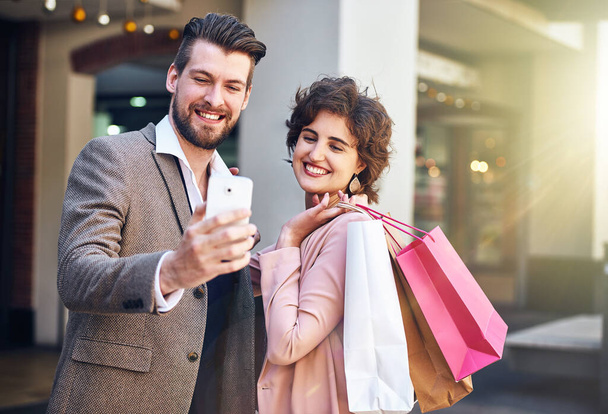 Why not spoil your selfie. Shot of a young couple taking a selfie while out shopping. - 写真・画像