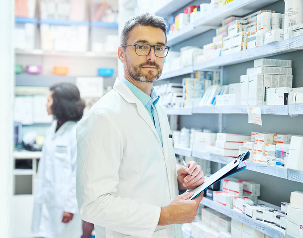 Medication is my expertise. Shot of a mature man doing inventory in a pharmacy with his colleague in the background. - Photo, Image