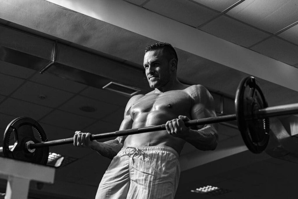 Muscular man doing crossfit. Fit man doing biceps lifting barbell. Young man working out at crossfit gym. Athletic guy doing exercise. - Photo, Image