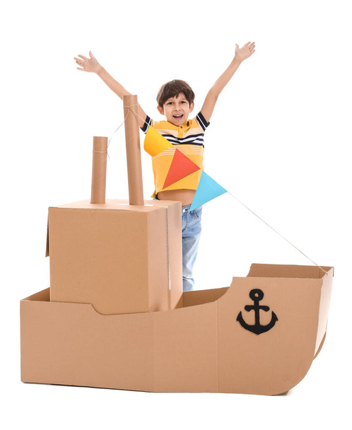 Cute little boy playing with cardboard ship on white background - Fotoğraf, Görsel