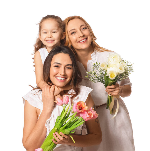 Jeune femme, sa petite fille et sa mère avec des fleurs sur fond blanc. Célébration de la Journée internationale de la femme - Photo, image
