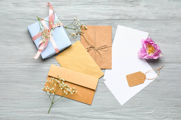 Blanko-Karten mit Umschlägen, Blumen und Geschenkschachtel auf grauem Holzgrund - Foto, Bild