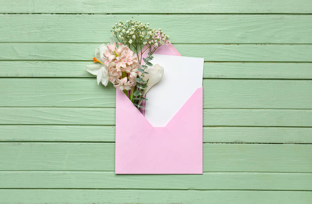 Envelope with card and flowers on green wooden background - 写真・画像