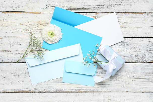 Envelopes with card, gift and flowers on white wooden background - Photo, Image