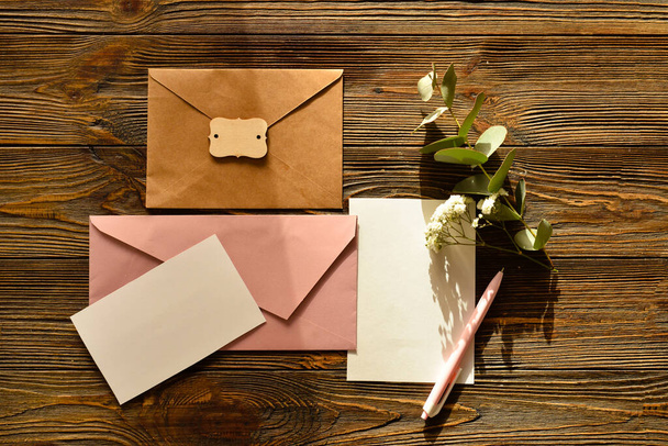 Envelopes with blank cards, flowers and eucalyptus branch on wooden background - Photo, Image