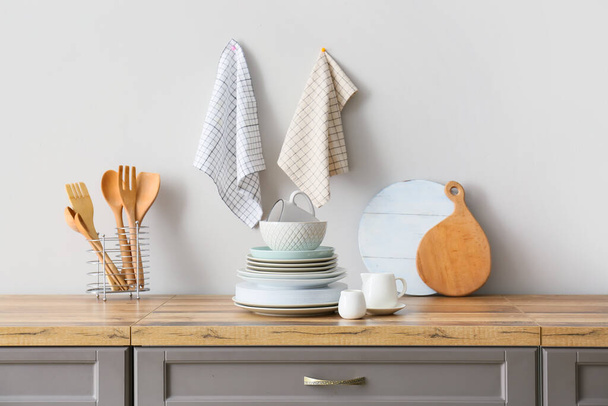 Beautiful dinnerware and kitchen utensils on counter near light wall - 写真・画像