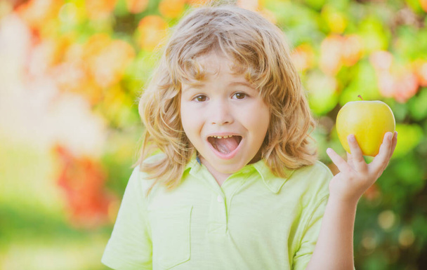 Happy little boy eating green apple. Smiling child holding and eats fresh apple, garden background. Portrait of cute happy child bites apple. - Fotoğraf, Görsel
