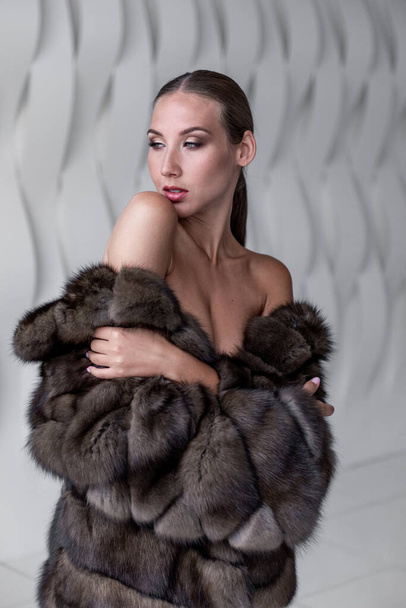 La belle femme a été enveloppée dans la fourrure moelleuse d'un manteau de fourrure est photographiée en studio blanc. Style commercial - Photo, image