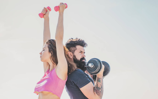Fit sexy couple on sky background with dumbbells. Fitness concept. Sports couple training with dumbbell. Healthy coupl life style. Sporty woman in sexy pink sportswear. - Φωτογραφία, εικόνα