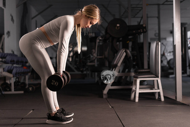 young caucasian girl in the gym doing an exercise for the back with dumbbells deadlift. copy space. - Photo, Image
