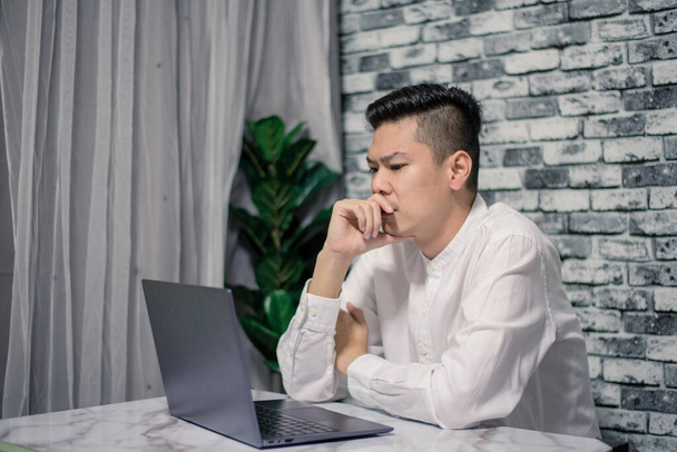 Portré fiatal férfi gondolkodás, miközben komolyan dolgozik otthon laptop az asztalon - Fotó, kép