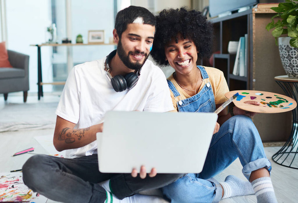 Internet está lleno de actividades divertidas para parejas. Fotografía de una pareja joven usando un ordenador portátil mientras pintaba en casa. - Foto, imagen