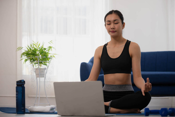 Poranna joga z Azjatką, siedzącą w pozycji Easy, postawy Sukhasana i medytującą online. - Zdjęcie, obraz