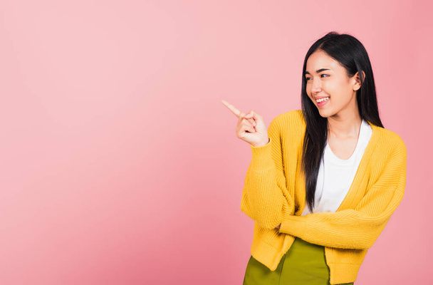 Asian happy portrait beautiful cute young woman standing pointing finger side away presenting product looking to away side, studio shot isolated on pink background with copy space - Foto, Imagen