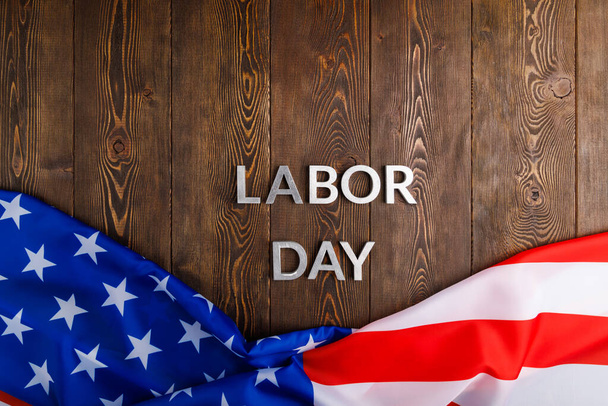 words labor day laid with silver metal letters on wooden surface with crumpled USA flag on bottom side - Photo, image