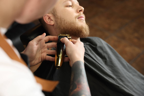 Professional hairdresser working with bearded client in barbershop, closeup - Фото, зображення