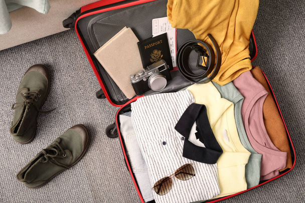 Open suitcase with clothes, accessories and shoes on floor, flat lay - Foto, imagen